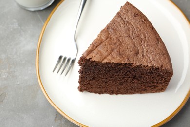 Photo of Piece of tasty chocolate sponge cake served on grey table, closeup