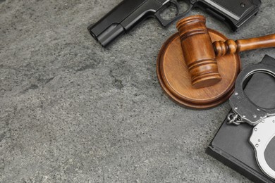 Book, judge's gavel, gun and handcuffs on gray textured table, flat lay. Space for text