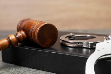 Book, judge's gavel and handcuffs on gray textured table, closeup