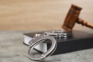 Book, judge's gavel and handcuffs on gray textured table, closeup