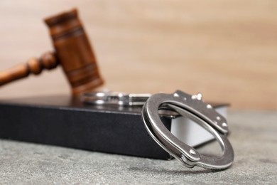 Book, judge's gavel and handcuffs on gray textured table, closeup