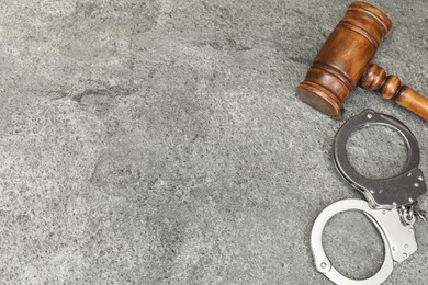 Photo of Judge's gavel and handcuffs on gray textured table, flat lay. Space for text