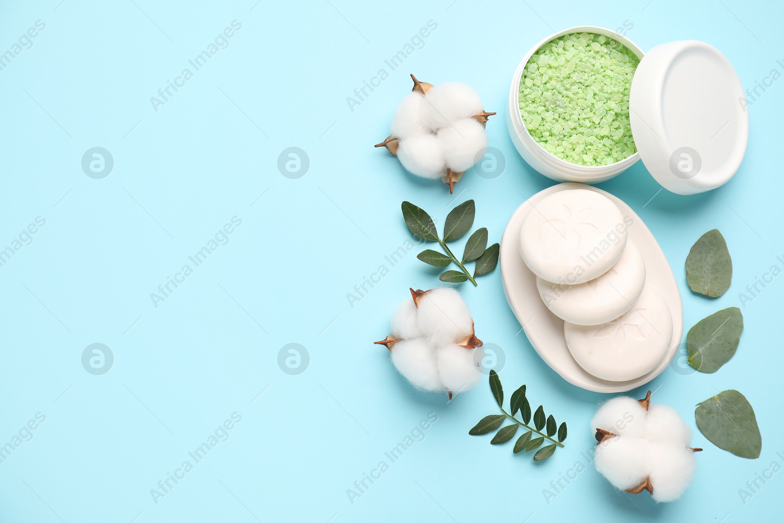 Photo of Different cosmetic products, green leaves and cotton flowers on light blue background, flat lay. Space for text