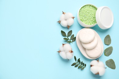 Different cosmetic products, green leaves and cotton flowers on light blue background, flat lay. Space for text