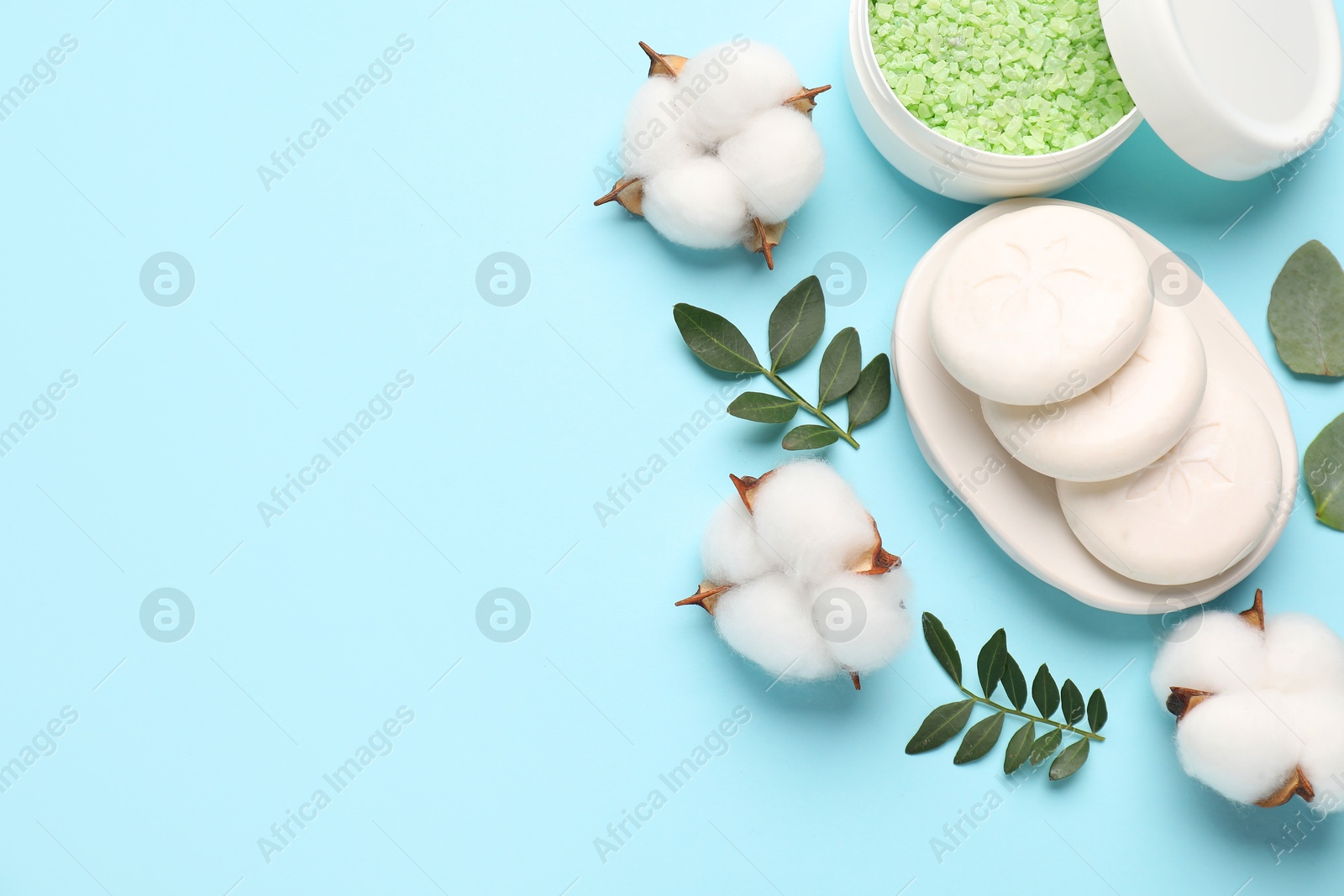 Photo of Different cosmetic products, green leaves and cotton flowers on light blue background, flat lay. Space for text