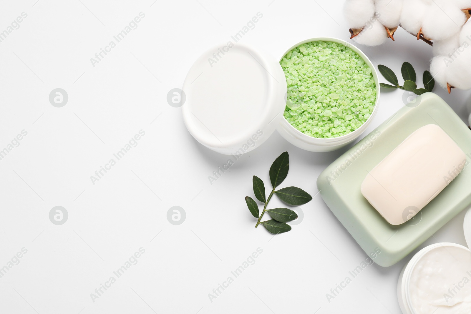 Photo of Different cosmetic products, cotton flowers and green leaves on white background, flat lay. Space for text