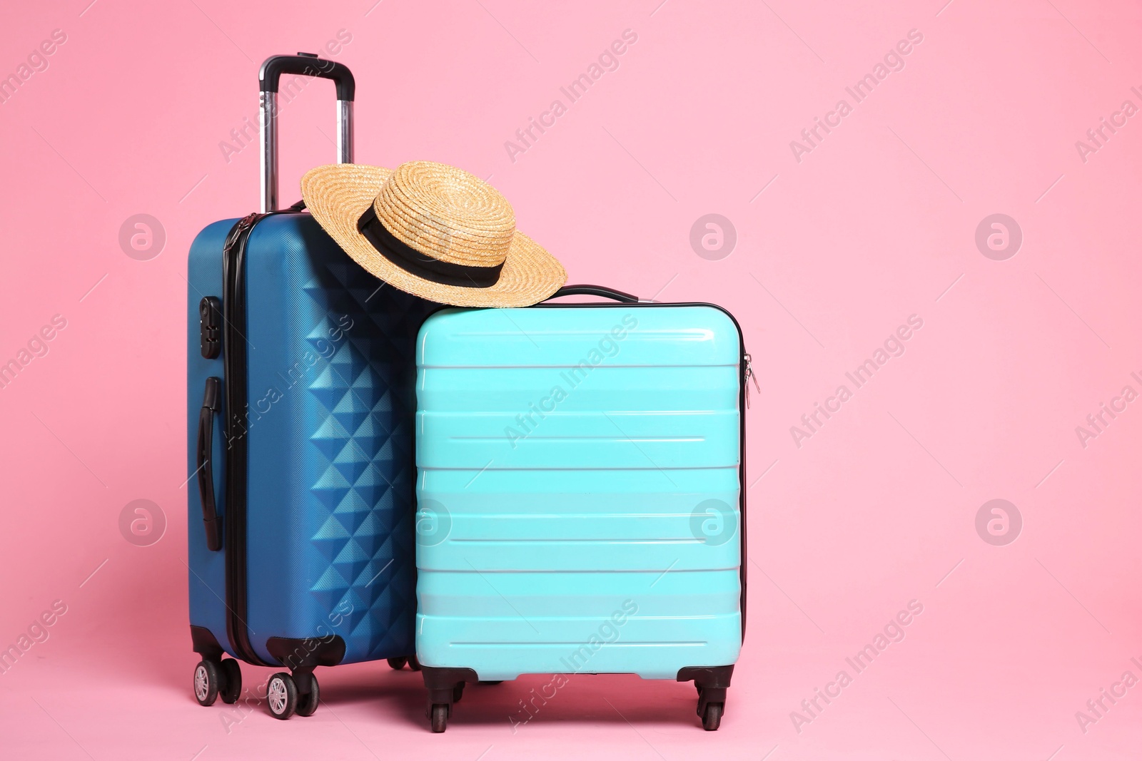 Photo of Two new color suitcases and wicker hat on pink background, space for text