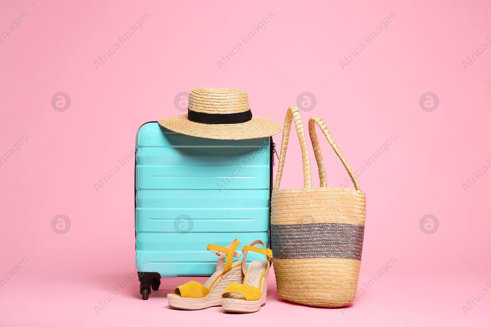 Photo of Turquoise suitcase, wicker hat, bag and shoes on pink background