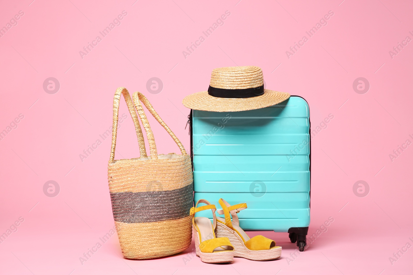 Photo of Turquoise suitcase, wicker hat, bag and shoes on pink background