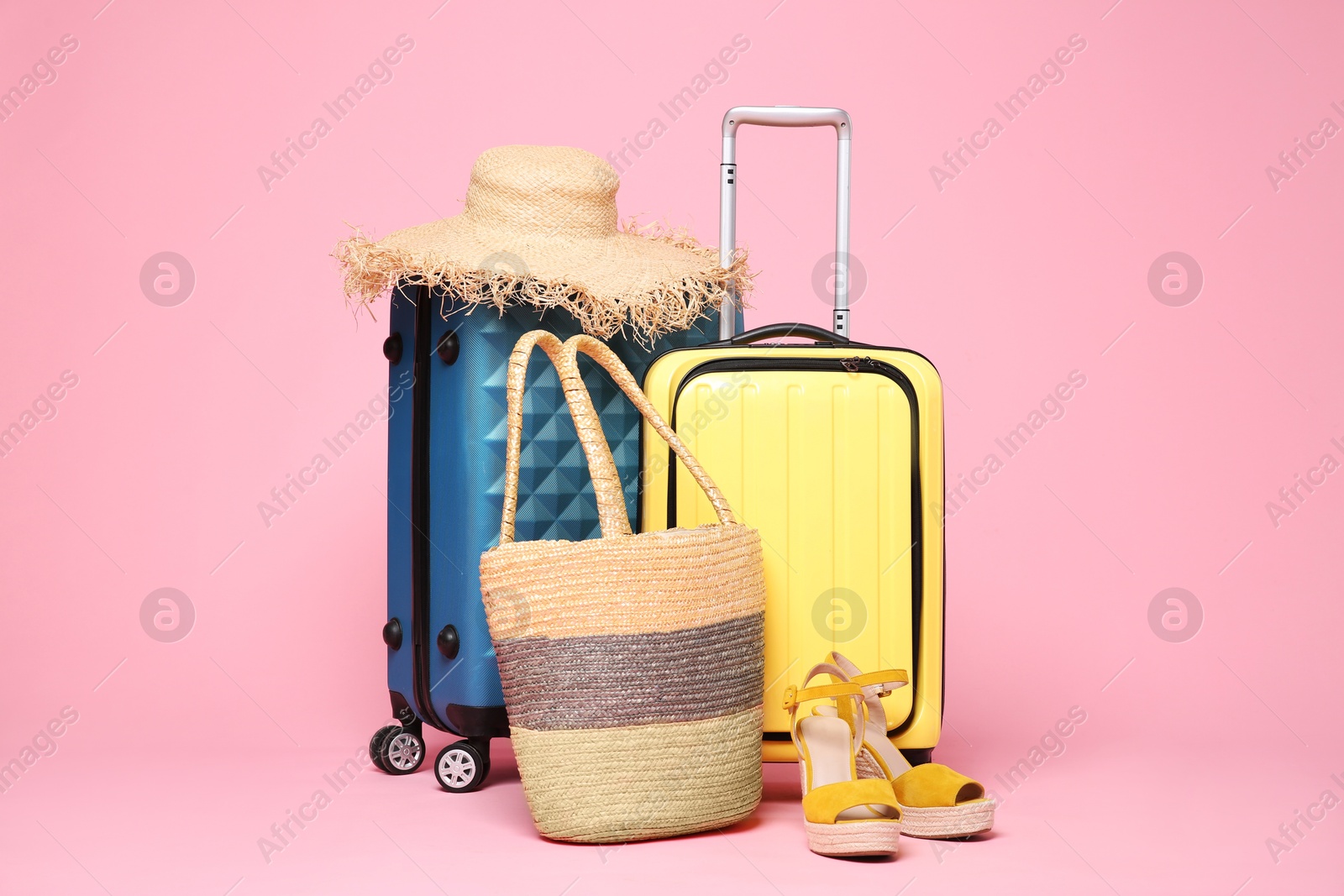 Photo of Two suitcases, straw hat, bag and shoes on pink background