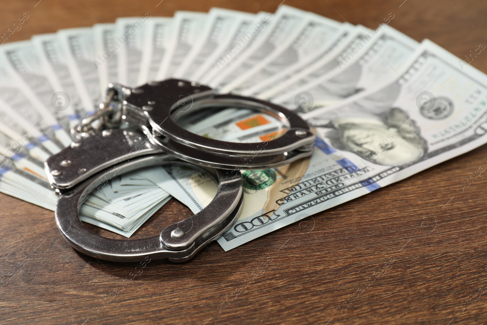 Photo of Handcuffs with dollar banknotes on wooden table, closeup