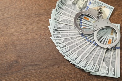 Photo of Handcuffs with dollar banknotes on wooden table, above view. Space for text