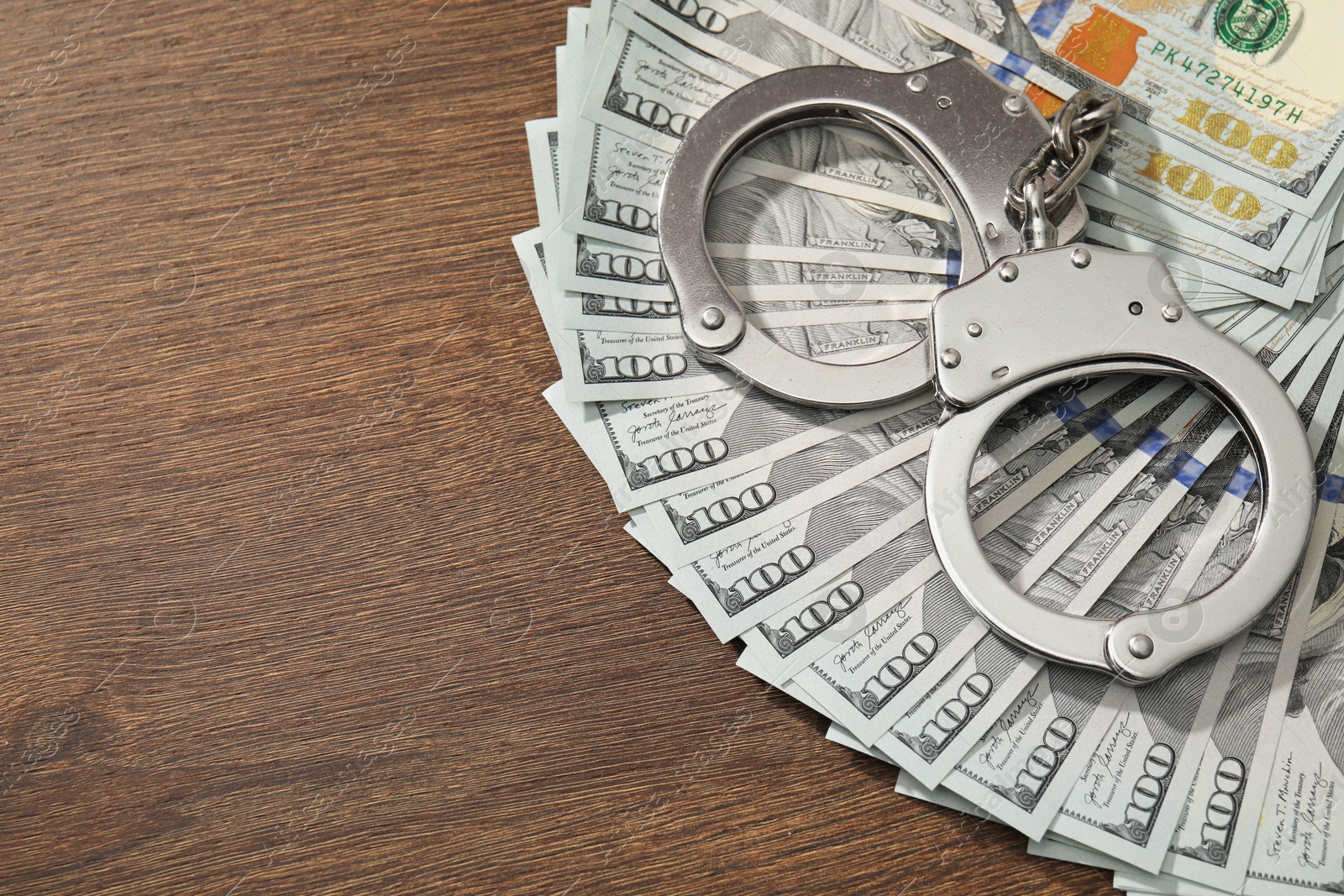 Photo of Handcuffs with dollar banknotes on wooden table, above view. Space for text