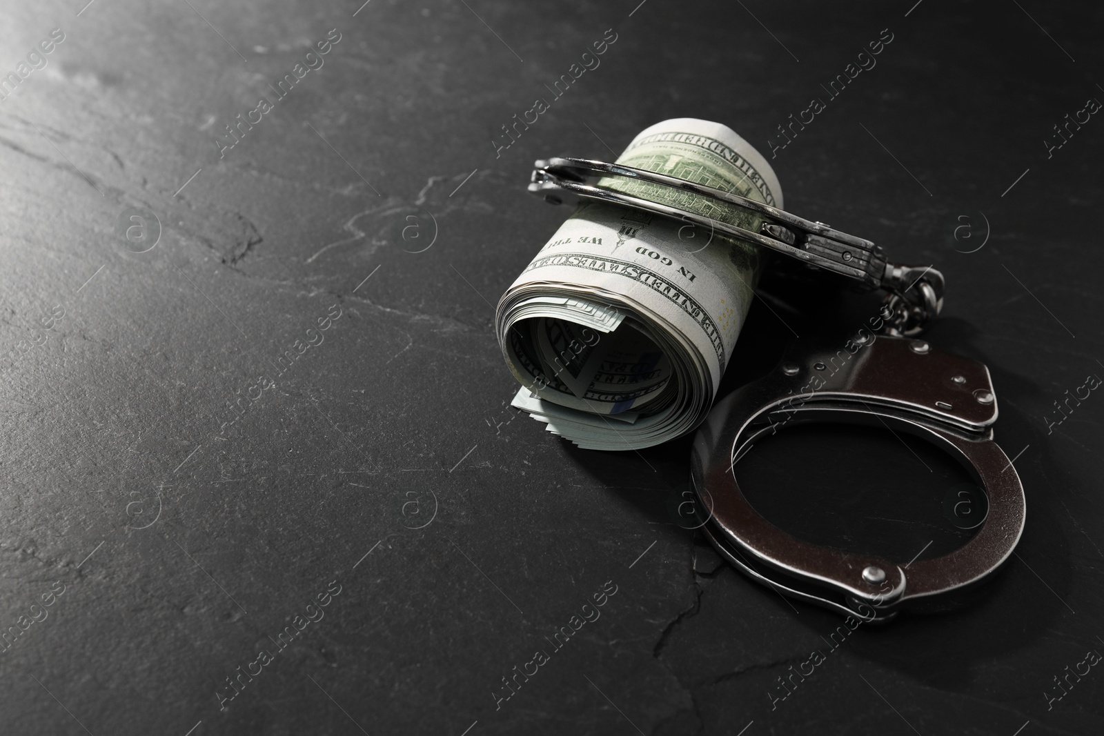 Photo of Handcuffs with dollar banknotes on grey textured table, space for text