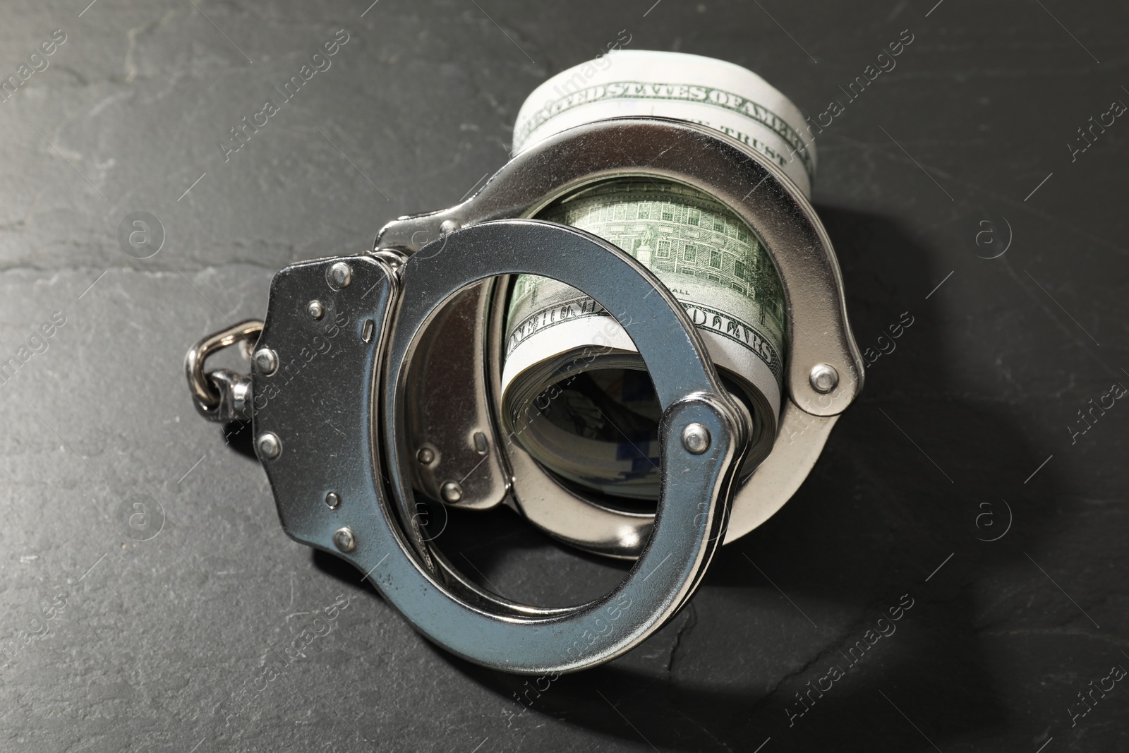 Photo of Handcuffs with dollar banknotes on grey textured table, closeup