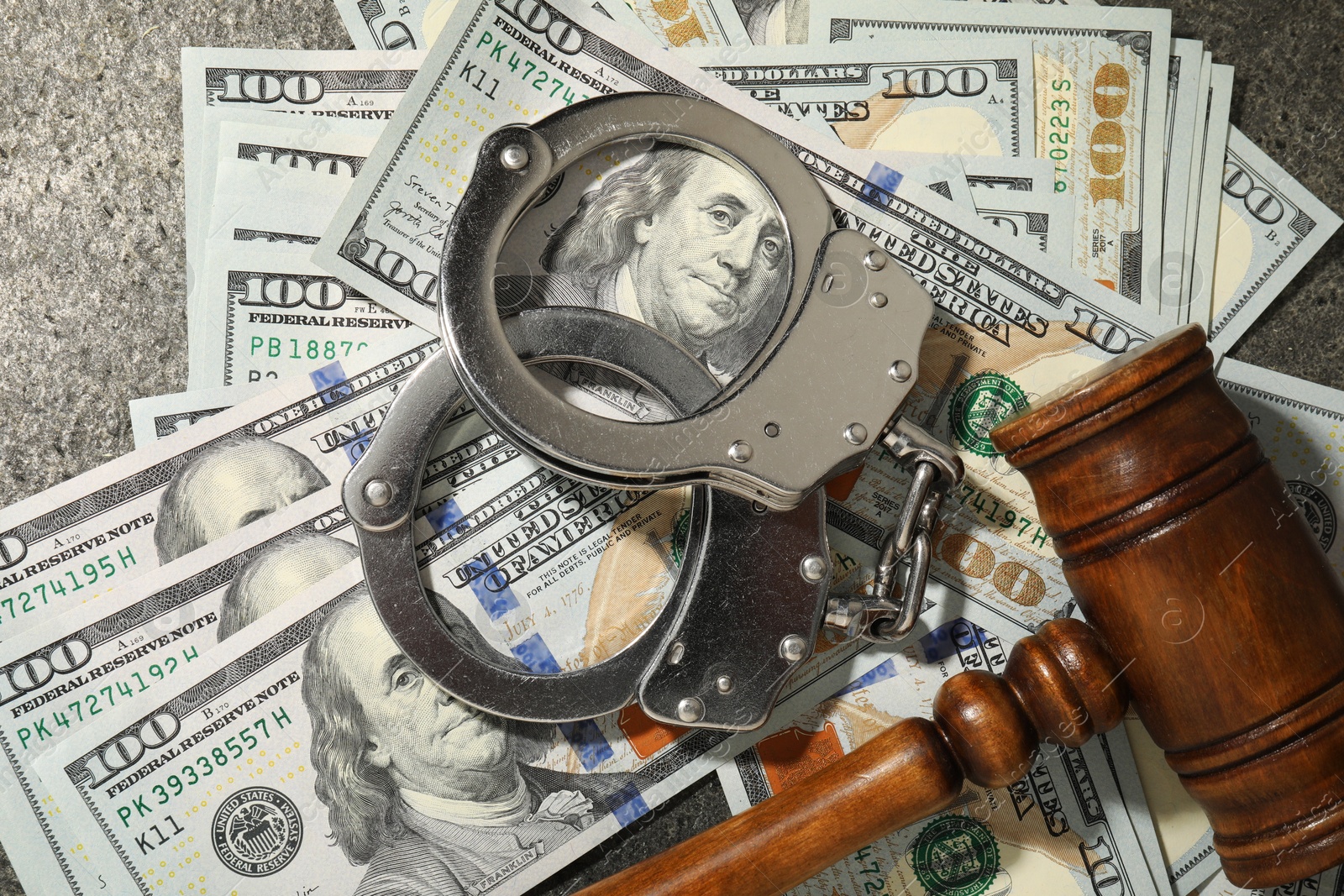 Photo of Handcuffs with dollar banknotes and wooden gavel on grey textured table, flat lay