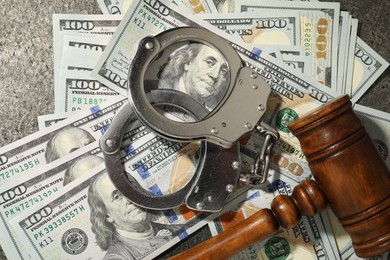 Handcuffs with dollar banknotes and wooden gavel on grey textured table, flat lay