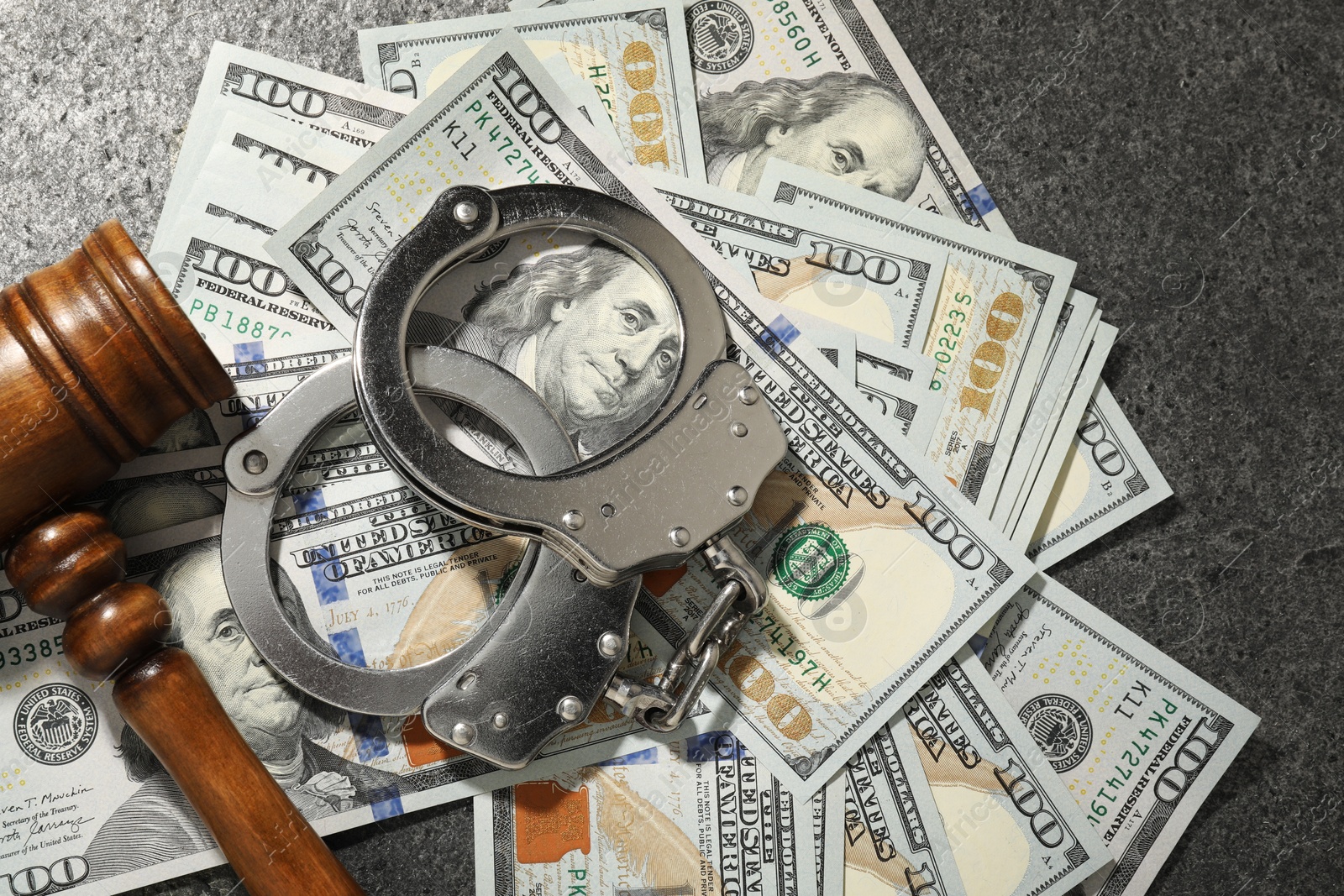 Photo of Handcuffs with dollar banknotes and wooden gavel on grey textured table, flat lay