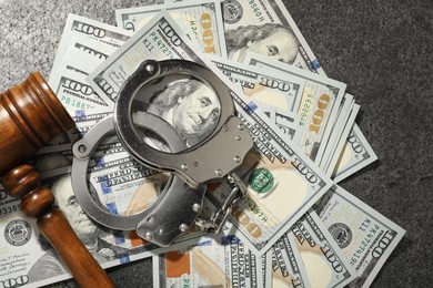 Handcuffs with dollar banknotes and wooden gavel on grey textured table, flat lay