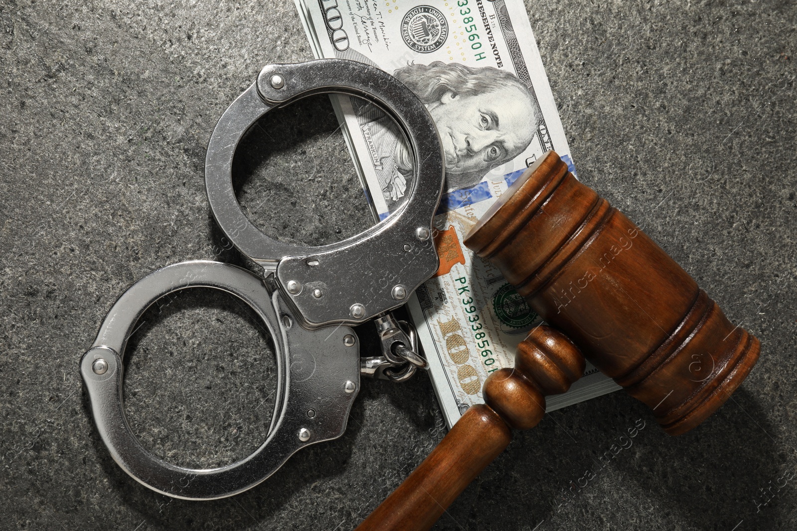 Photo of Handcuffs with dollar banknotes and wooden gavel on grey textured table, flat lay