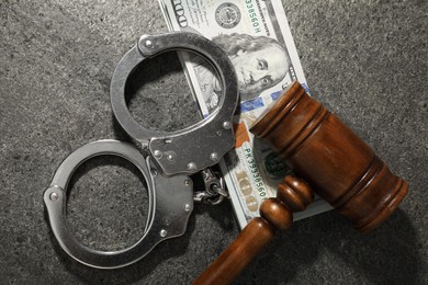 Handcuffs with dollar banknotes and wooden gavel on grey textured table, flat lay