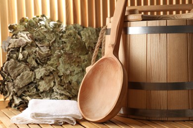 Photo of Sauna equipment. Bucket, oak whisk, towel and ladle on wooden surface