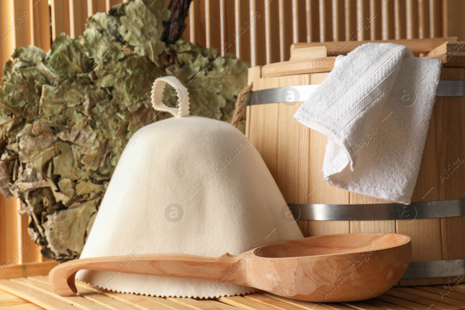 Photo of Sauna equipment. Bucket, ladle, towel, oak whisk and felt wool hat on wooden surface