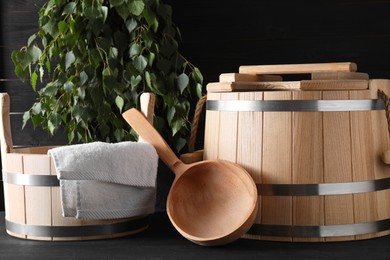 Photo of Sauna equipment. Wooden buckets, towel and ladle on black surface