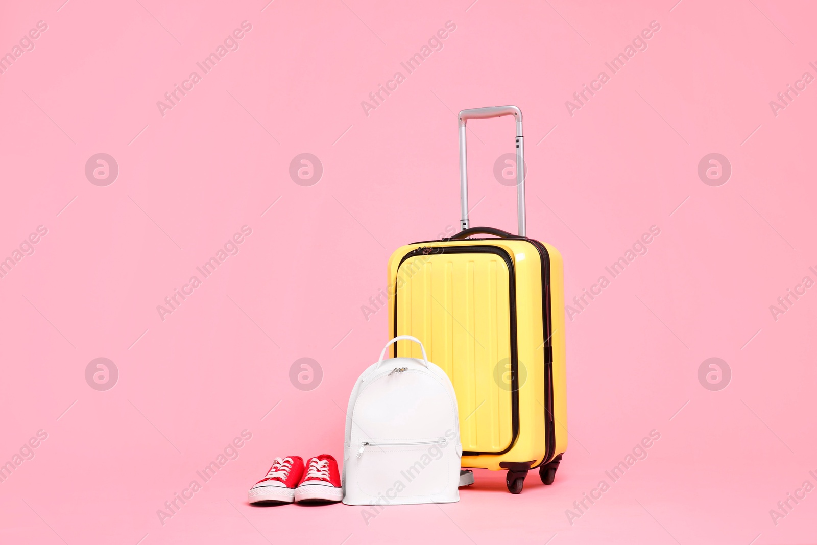 Photo of Yellow suitcase, sneakers and backpack on pink background