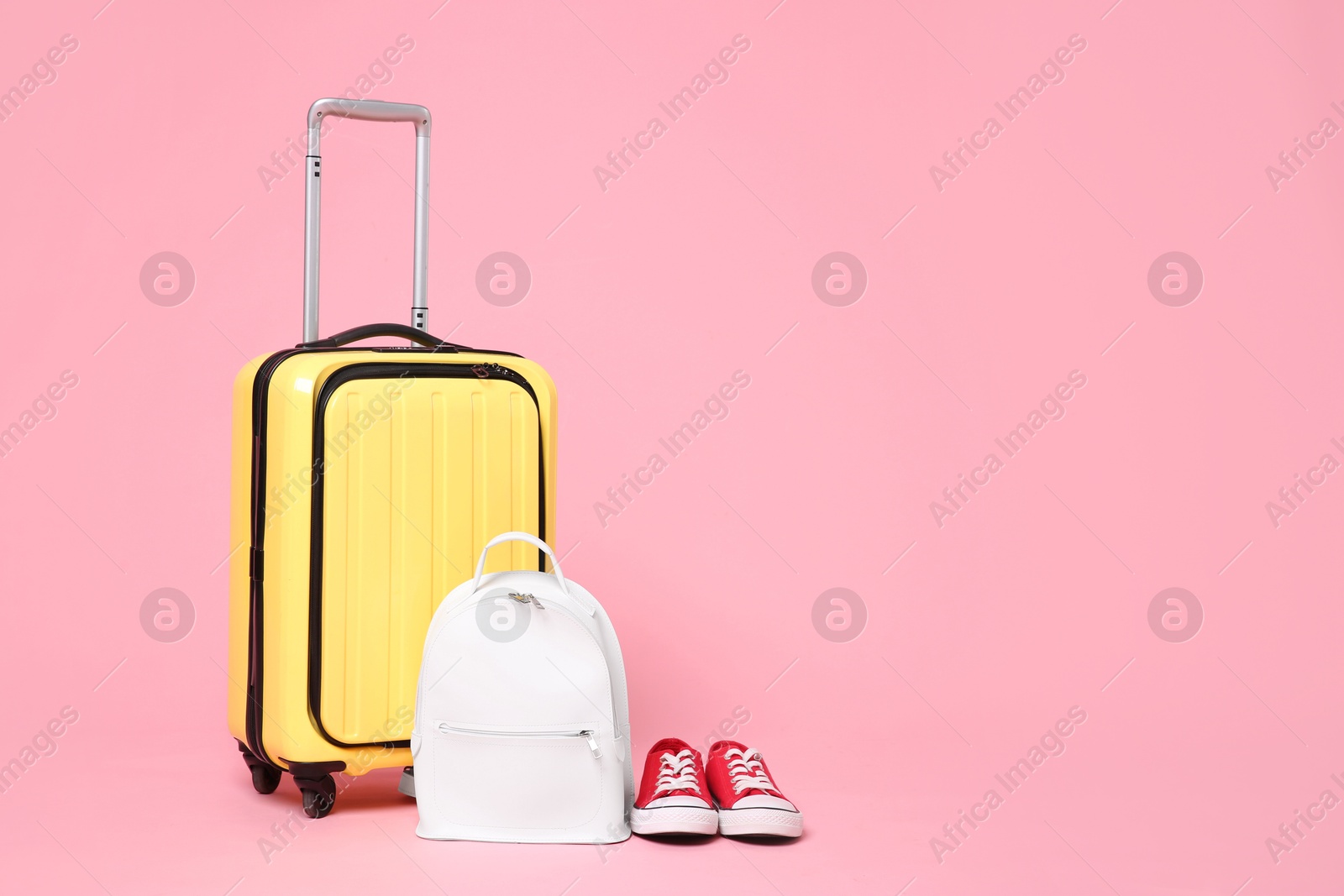 Photo of Yellow suitcase, sneakers and backpack on pink background, space for text