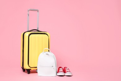 Photo of Yellow suitcase, sneakers and backpack on pink background, space for text