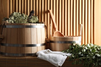 Photo of Sauna equipment. Buckets, whisks, ladle, and towel on bamboo bench near wooden wall