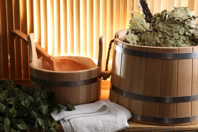 Sauna equipment. Buckets, whisks, ladle, and towel on bamboo bench against wooden wall