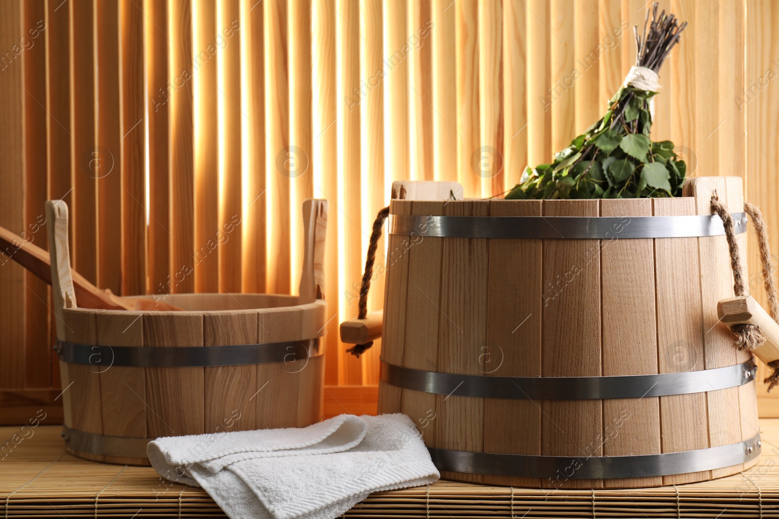 Photo of Sauna equipment. Buckets, birch whisk, ladle and towel on bamboo bench against wooden wall