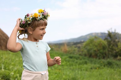 Portrait of smiling little girl in floral wreath at green meadow, space for text. Child enjoying beautiful nature