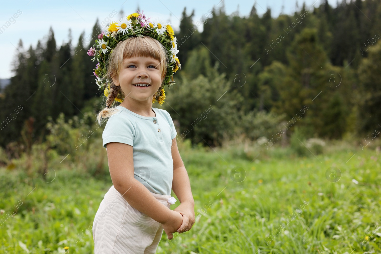 Photo of Portrait of smiling little girl in floral wreath at green meadow, space for text. Child enjoying beautiful nature