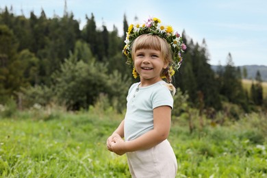 Photo of Portrait of smiling little girl in floral wreath at green meadow. Child enjoying beautiful nature