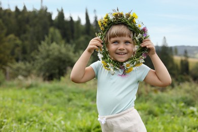 Photo of Portrait of smiling little girl with floral wreath at meadow, space for text. Child enjoying beautiful nature