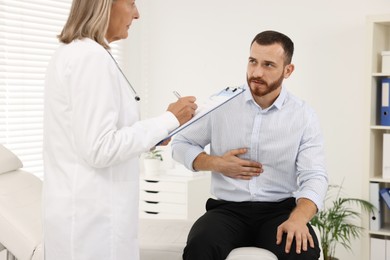 Doctor consulting patient with stomach pain in clinic, closeup