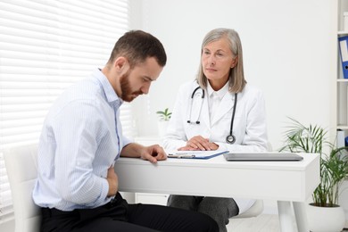 Photo of Doctor consulting patient with stomach pain at table in clinic