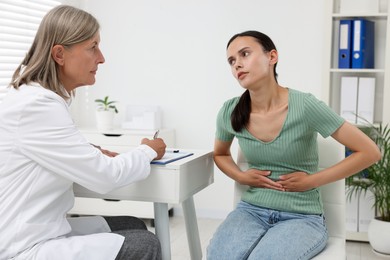 Photo of Doctor consulting patient with stomach pain at table in hospital