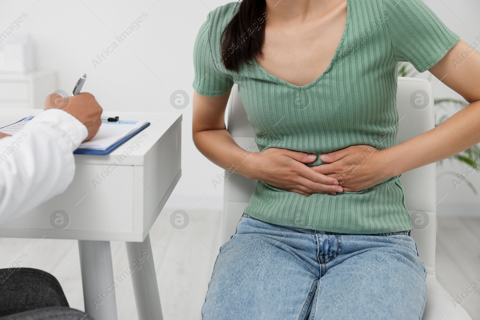 Photo of Doctor consulting patient with stomach pain at table in clinic, closeup