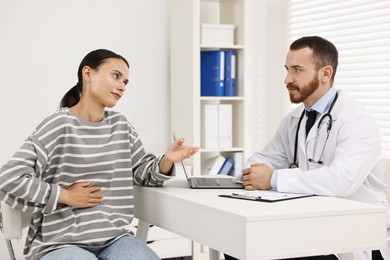 Photo of Doctor consulting patient with stomach pain at table in hospital