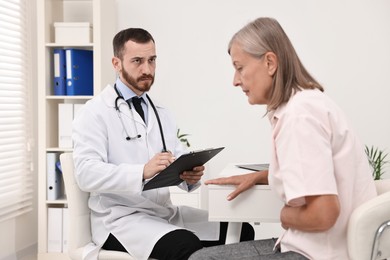 Photo of Doctor consulting senior patient with stomach pain at table in hospital