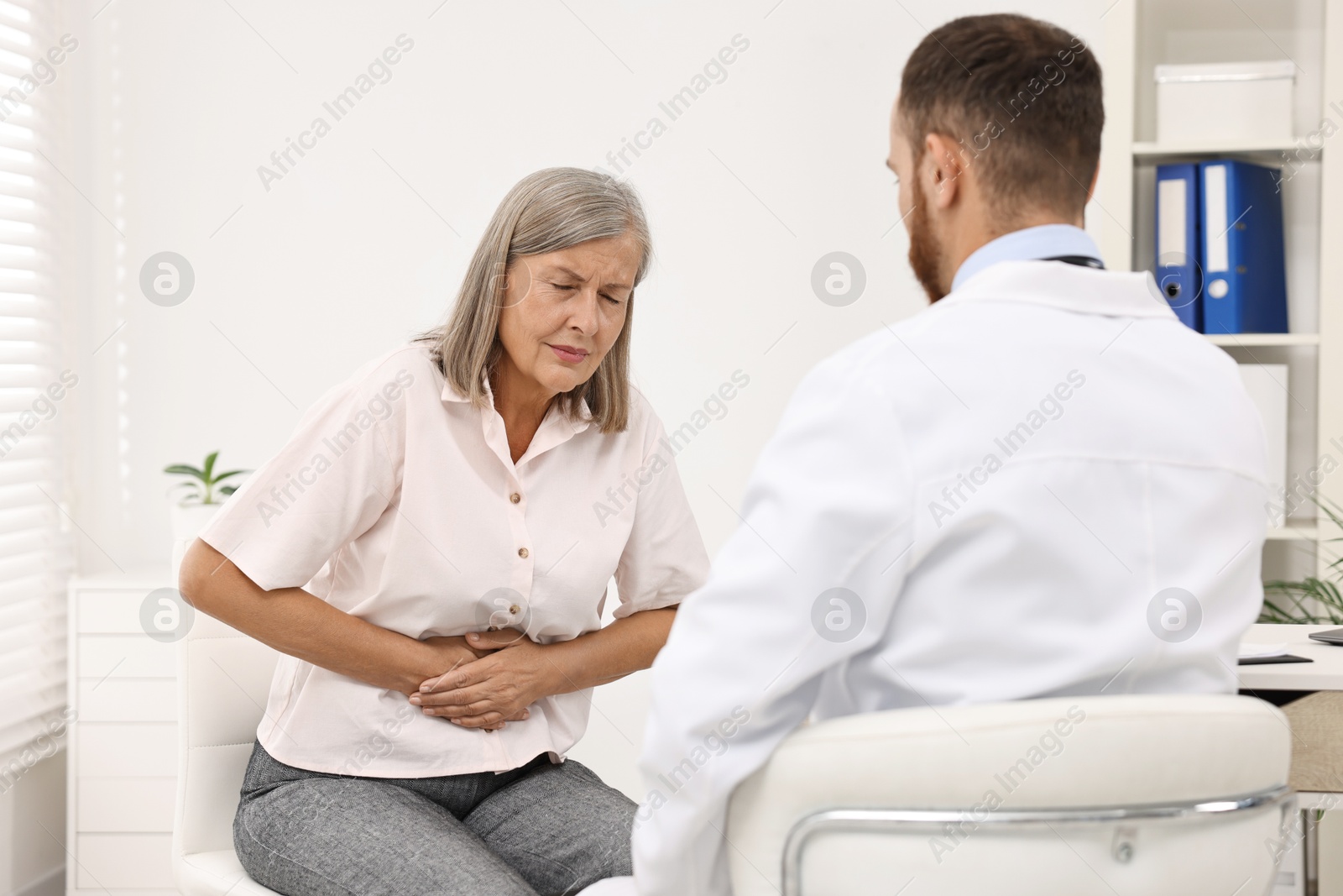 Photo of Doctor consulting senior patient with stomach pain in clinic, back view