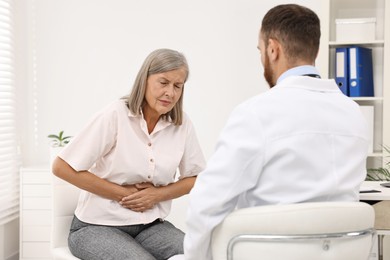 Photo of Doctor consulting senior patient with stomach pain in clinic, back view