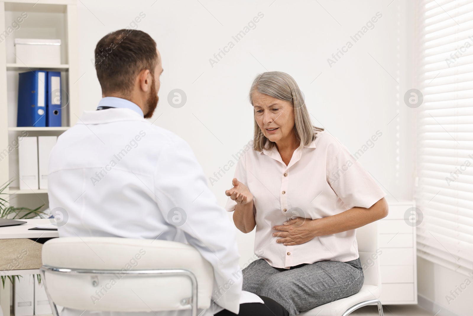 Photo of Doctor consulting senior patient with stomach pain in clinic, back view