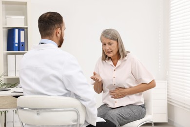 Doctor consulting senior patient with stomach pain in clinic, back view