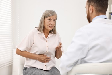 Doctor consulting senior patient with stomach pain in clinic, back view