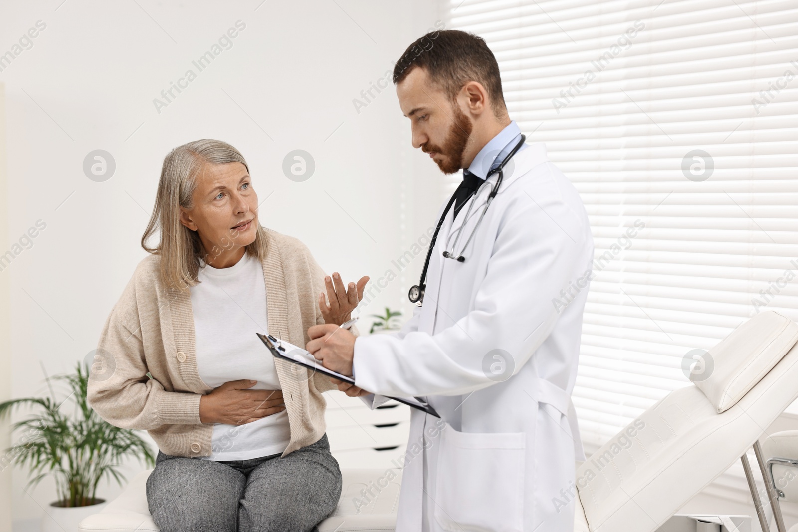 Photo of Doctor consulting senior patient with stomach pain in clinic